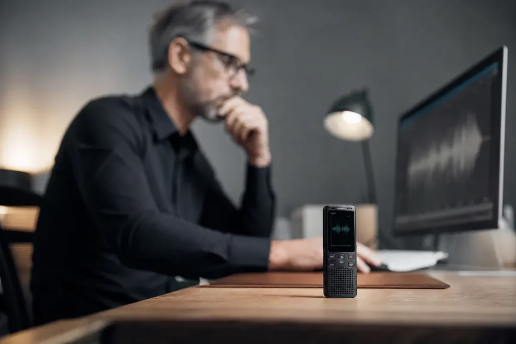 Mini registratore vocale su tavolo con forma d’onda audio visibile su schermo al computer