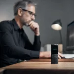 Mini registratore vocale su tavolo con forma d’onda audio visibile su schermo al computer