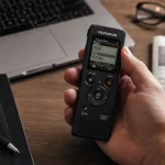 Registratore vocale digitale con schermata di impostazione data e ora su una scrivania professionale con laptop e accessori